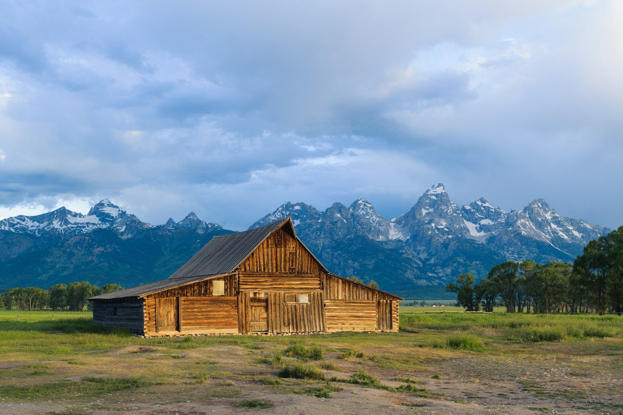 A weathered wooden barn in a meadow in Grand Teton National Park with the Teton Range behind it